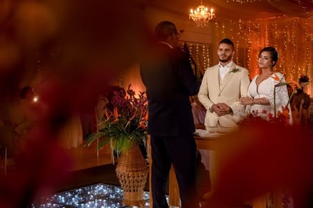 Noivos diante do celebrante durante a cerimônia de casamento, com flores em primeiro plano